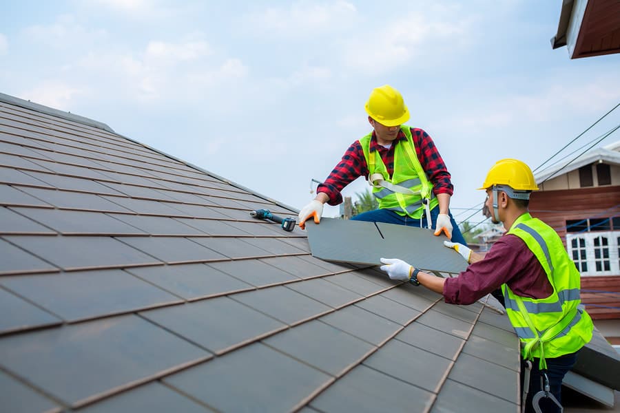 Two roofers installing shingles in high-visibility workwear